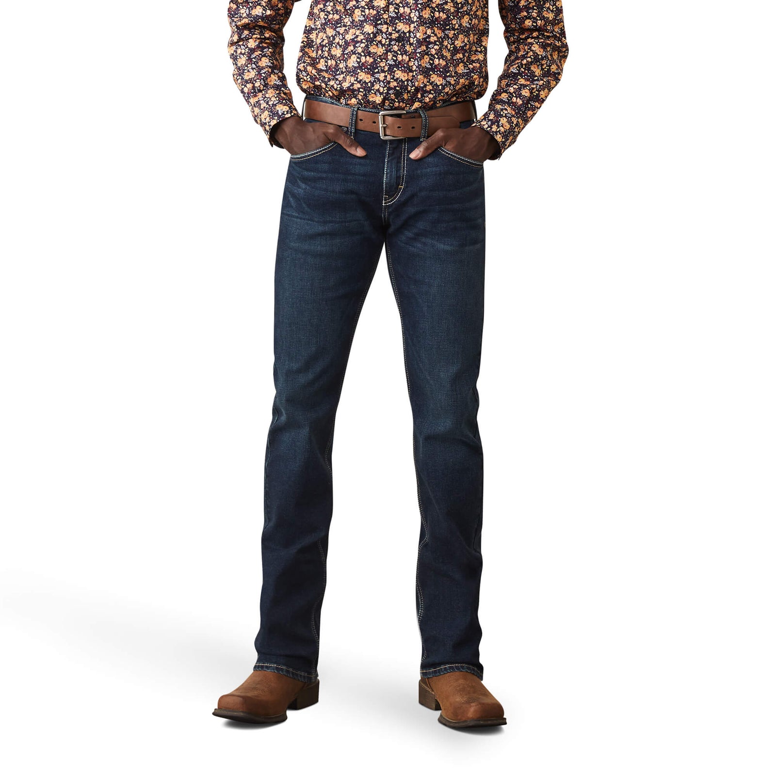 A man standing with hands in pockets wearing Ariat Men's Bryson M8 Straight Leg Jean, a brown belt, and brown boots.