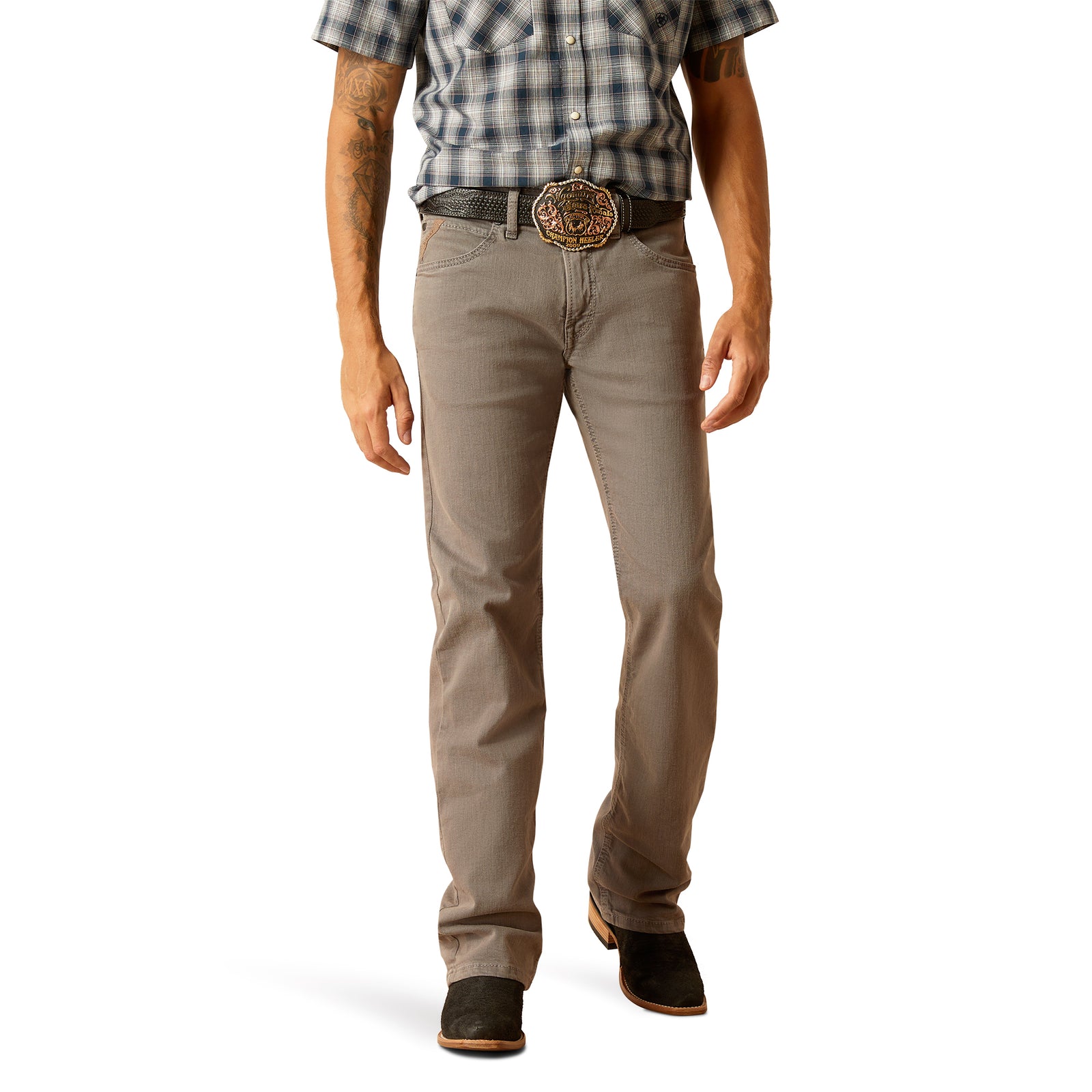 Ariat Men's M5 Hansen Straight Leg Jean. A man standing straight, wearing brown straight leg jeans and a checkered shirt with the sleeves rolled up. He has a belt with a prominent buckle and is feet are placed shoulder-width apart.