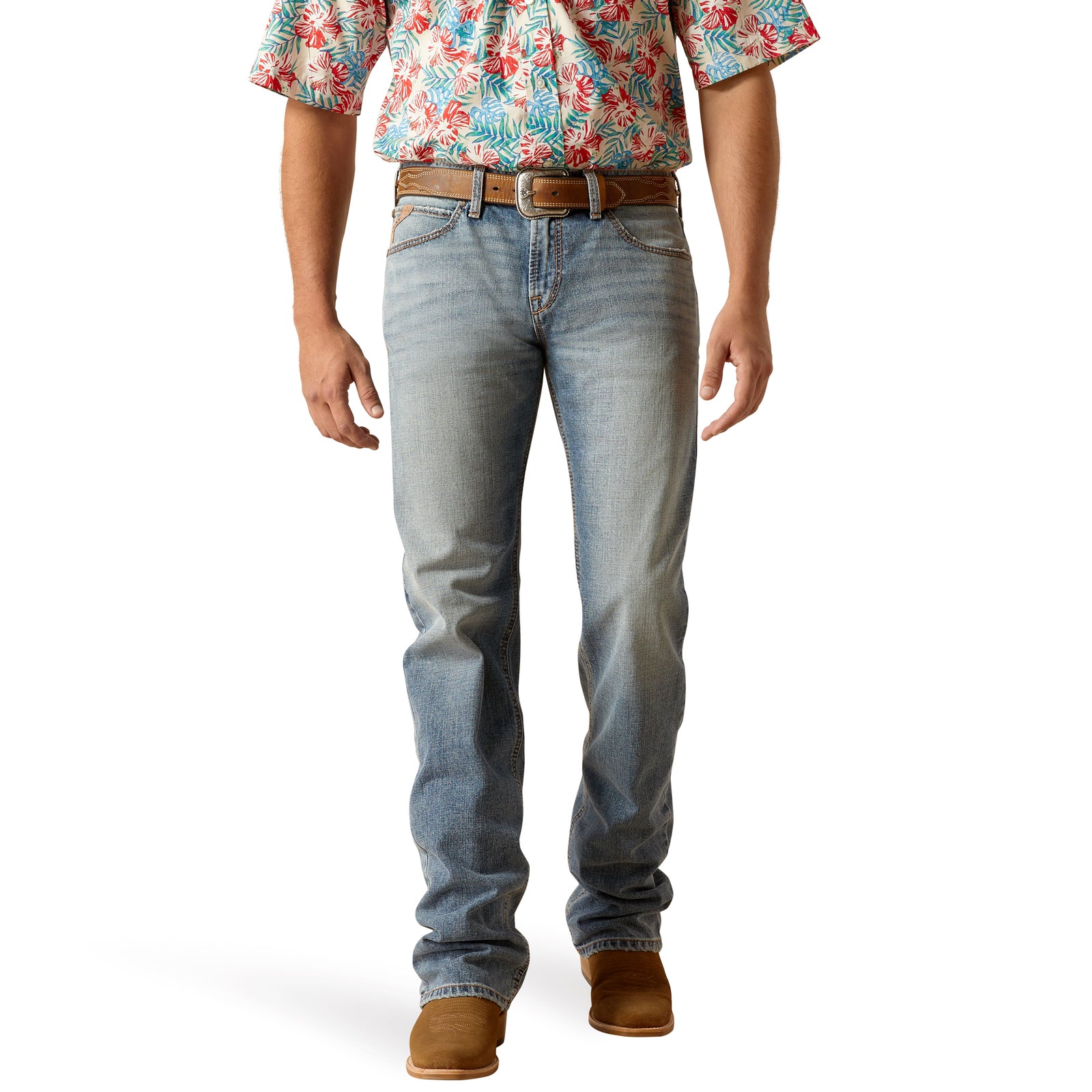 A man wearing a pair of Ariat M7 Deco Men's Straight Leg Jeans, which are slim through the seat and thigh with a low rise and straight leg opening. He is also wearing a floral shirt and brown shoes.