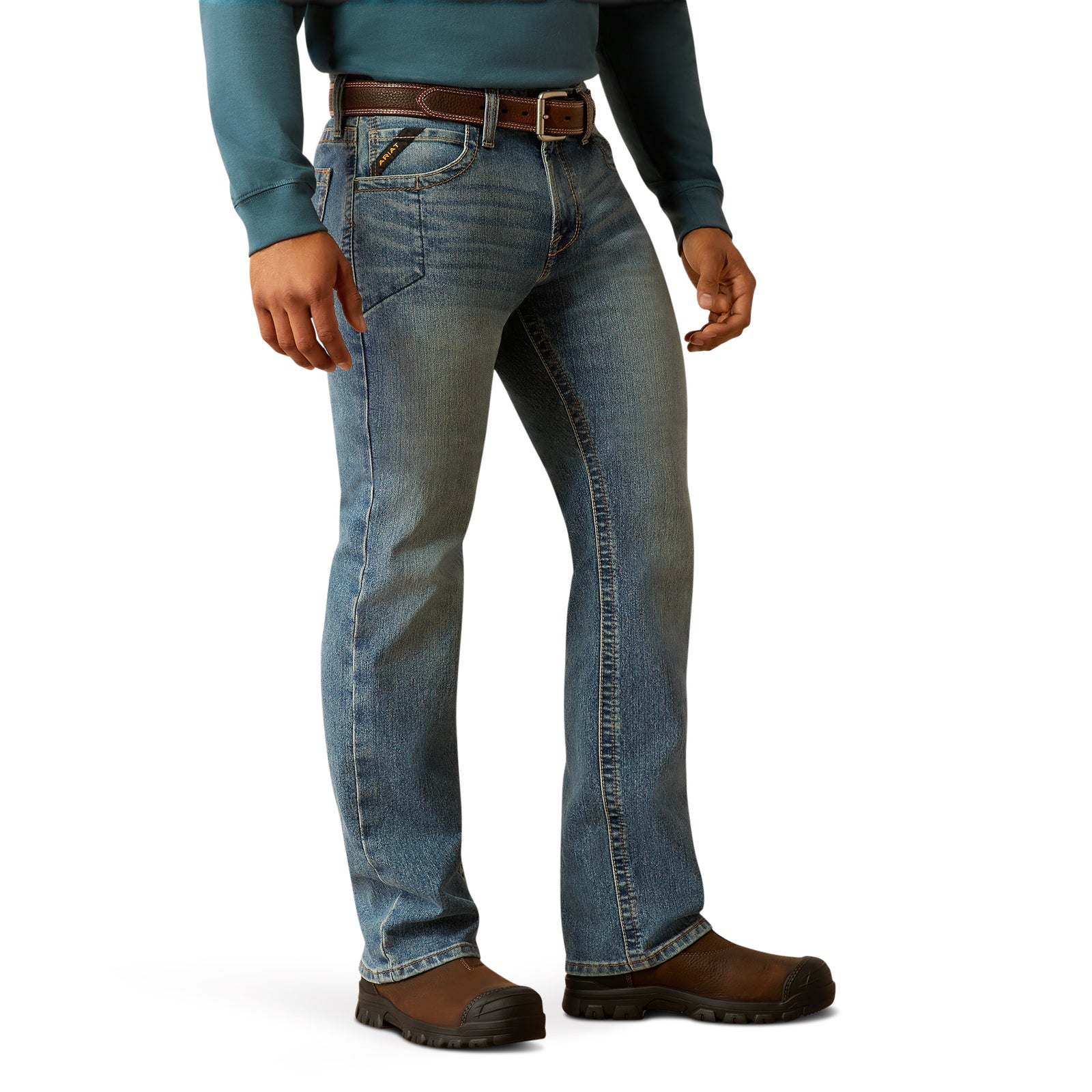A man standing wearing Ariat Men's Rebar M7 Rail Slim Straight Jean, a blue denim jean with a slim fit and a straight leg cut.