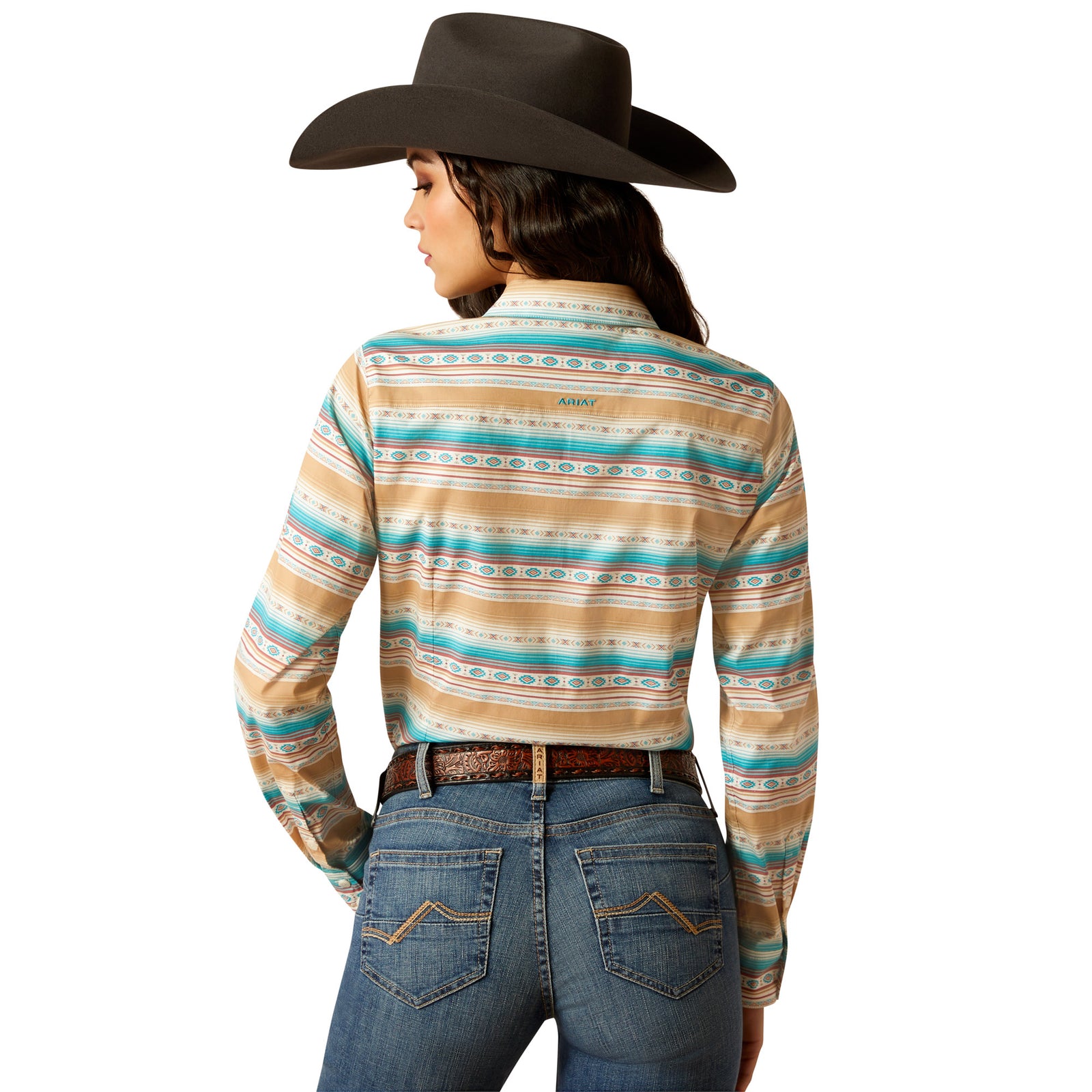Ariat Women's Wrinkle Resist Team Kirby Stretch Shirt. A woman wearing a long-sleeved striped shirt in beige, blue, and multicolor, with a cowboy hat and blue jeans.