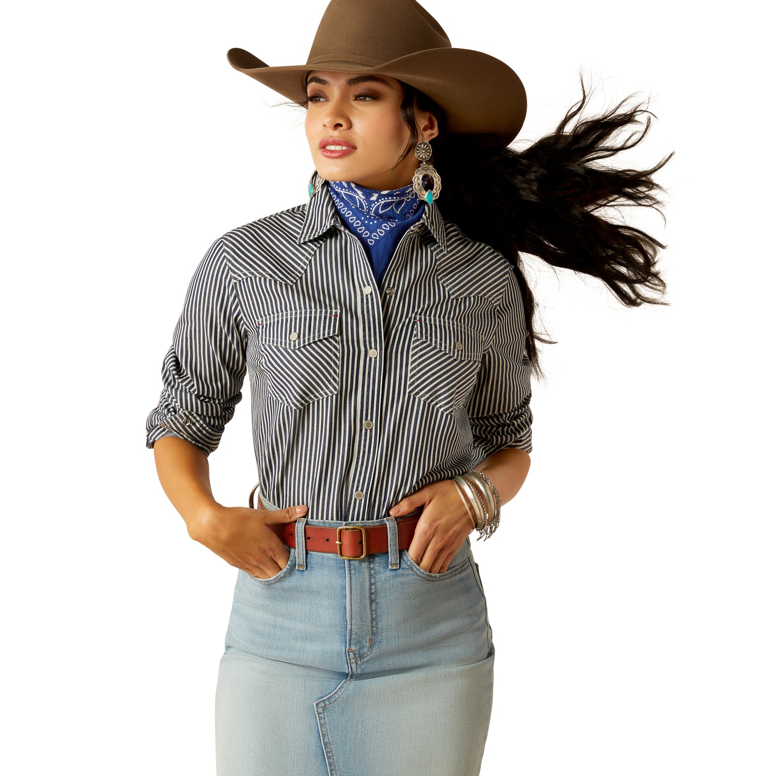 Ariat Women's Railroad Stripe L/S Western Shirt. A woman wearing a striped long-sleeve western shirt with snap-front closure and snap sleeve placket. She has a cowboy hat on and is standing against a white background.
