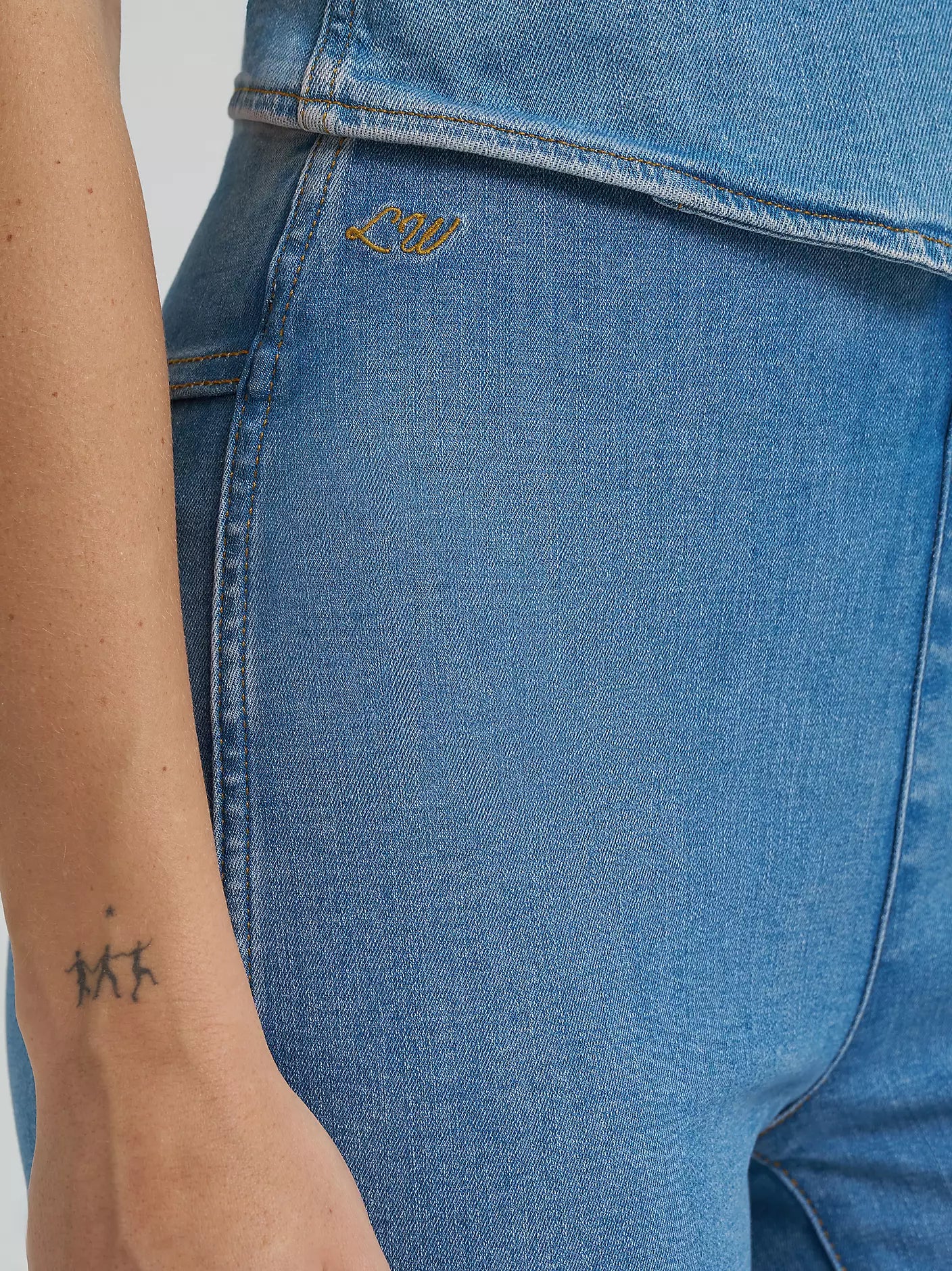 Close-up of blue jeans with a brand logo on the pocket, worn by a person.
