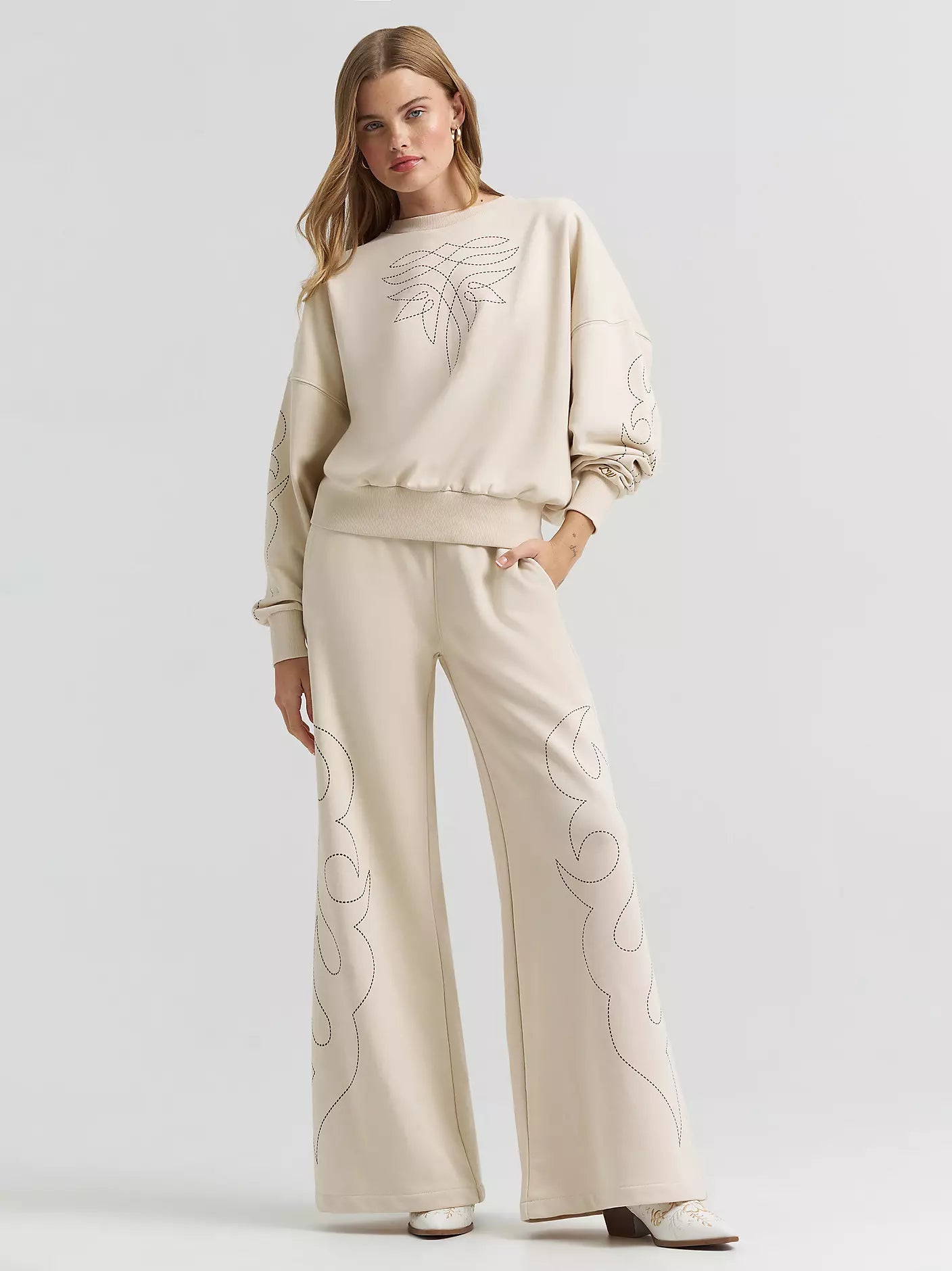 Woman wearing a beige embroidered outfit on a light gray background