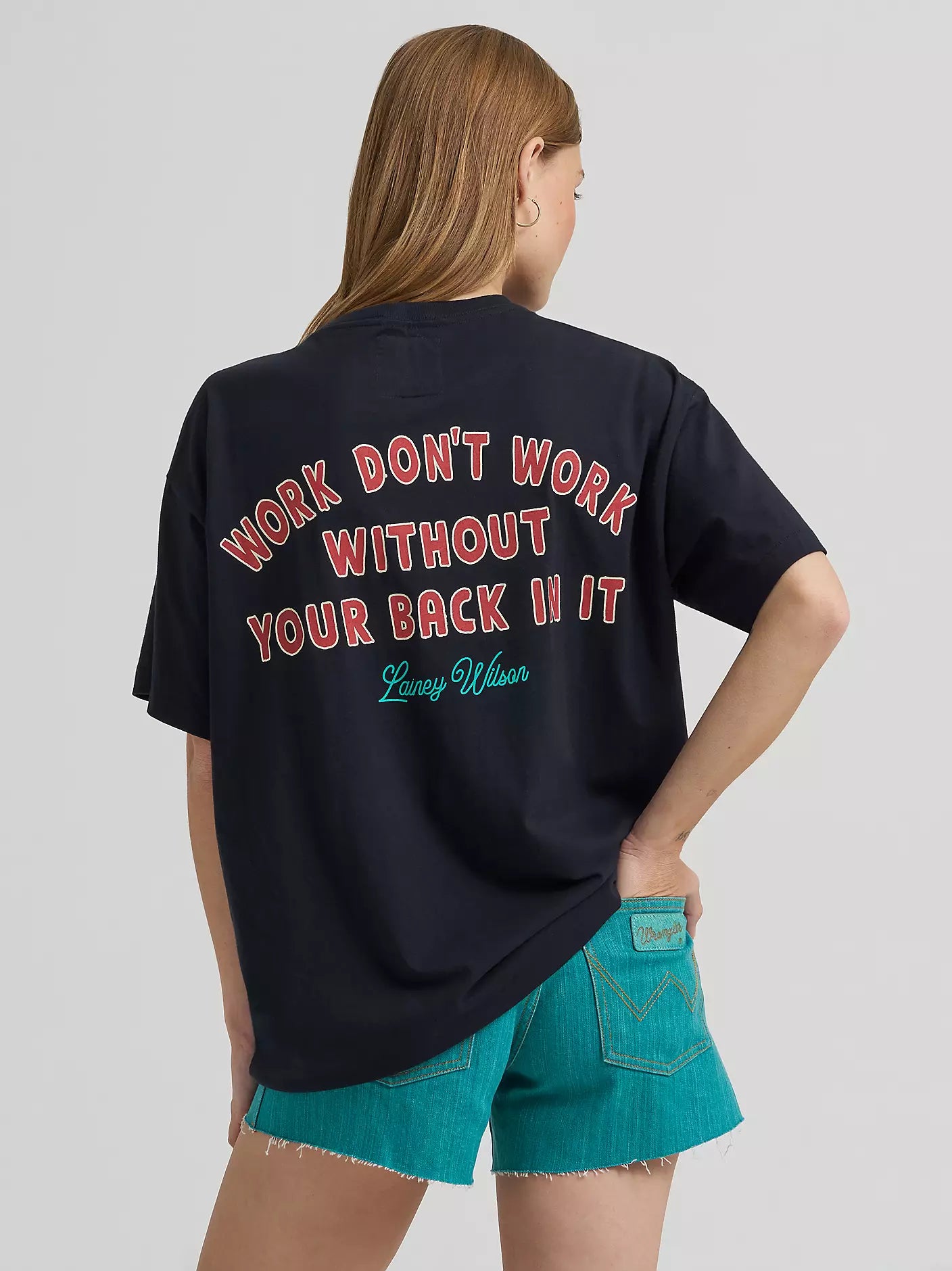 Person wearing a black t-shirt with text on the back, standing against a plain background