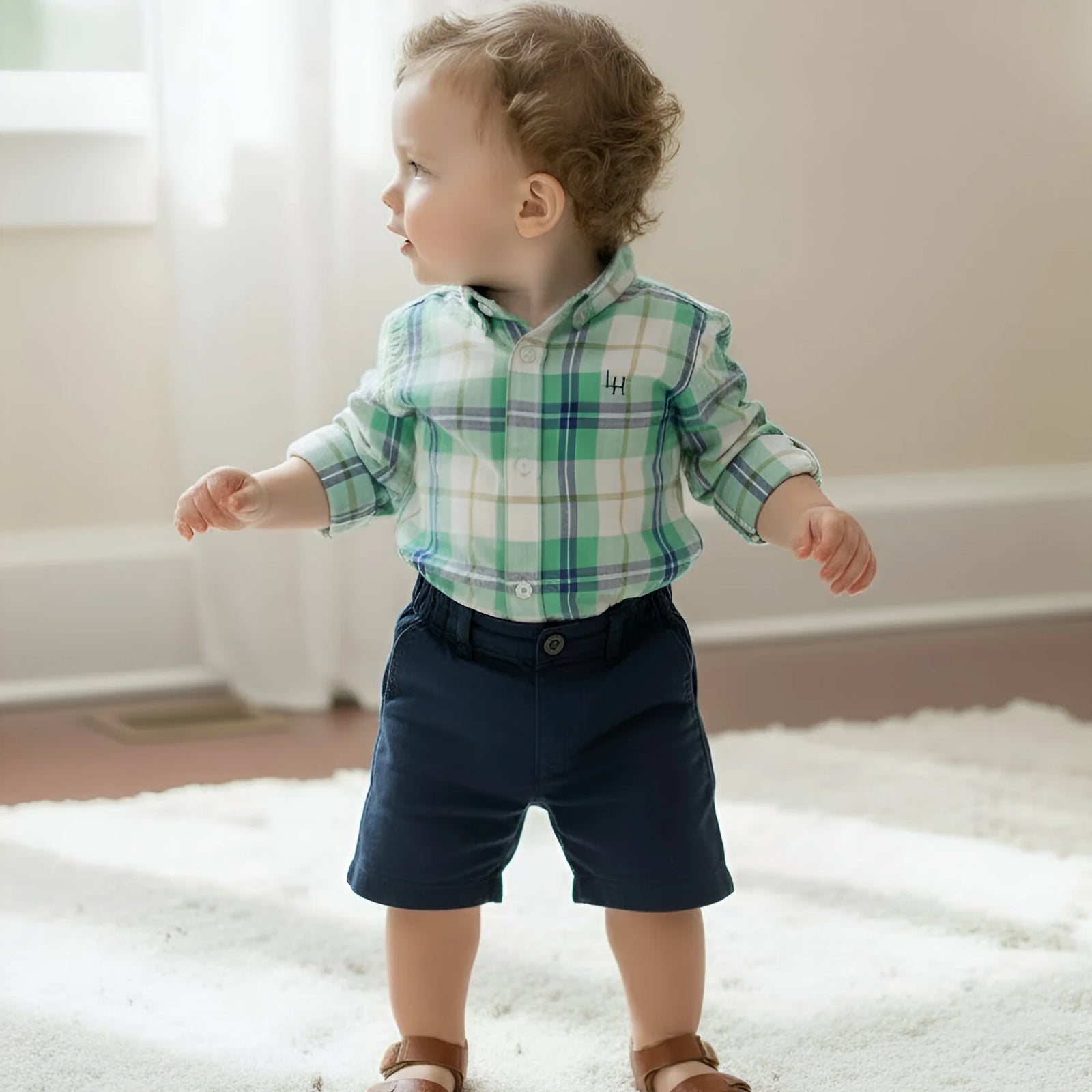 Child wearing a plaid shirt and navy shorts standing on a carpeted floor.