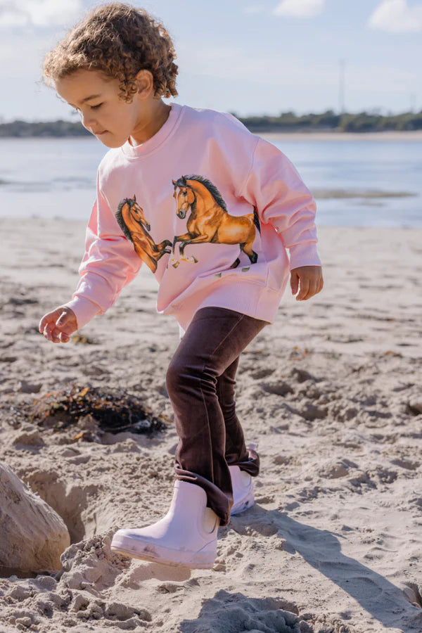 Child wearing a pink sweatshirt with horse designs on a beach