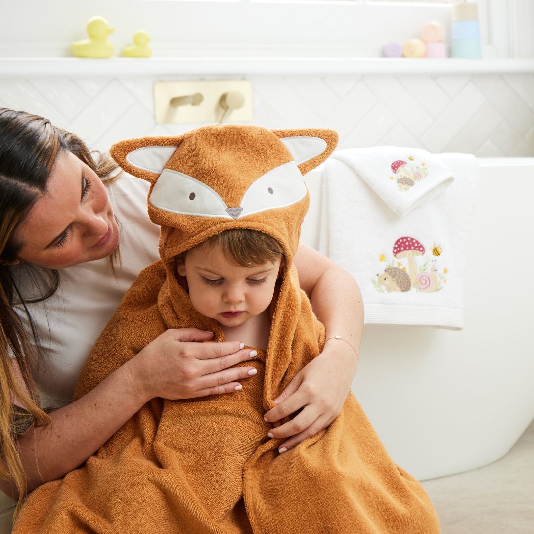Child wearing a fox-themed hooded towel being comforted by an adult in a bathroom setting.