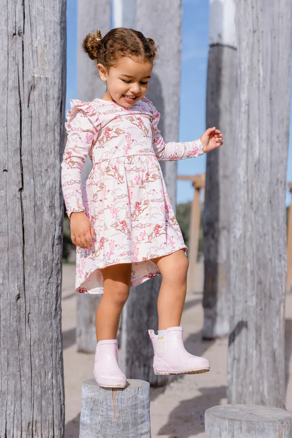 Young girl in a floral dress standing on wooden posts with a clear sky background