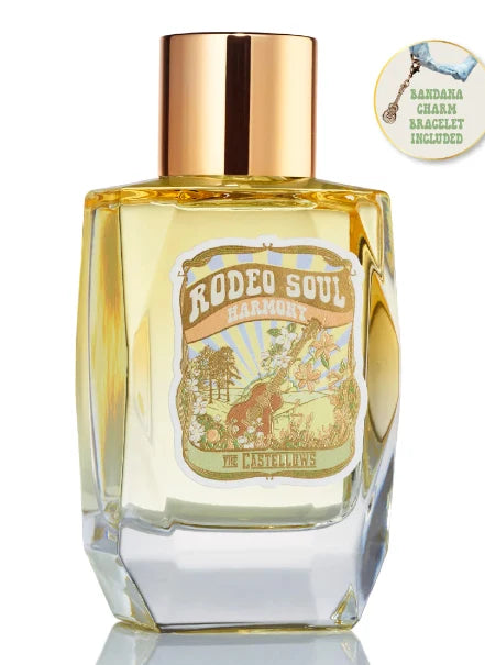 A faceted clear glass perfume bottle filled with pale golden-yellow liquid, topped with a metallic rose-gold cap. The front label reads 'Rodeo Soul Harmonix' with western-themed artwork.