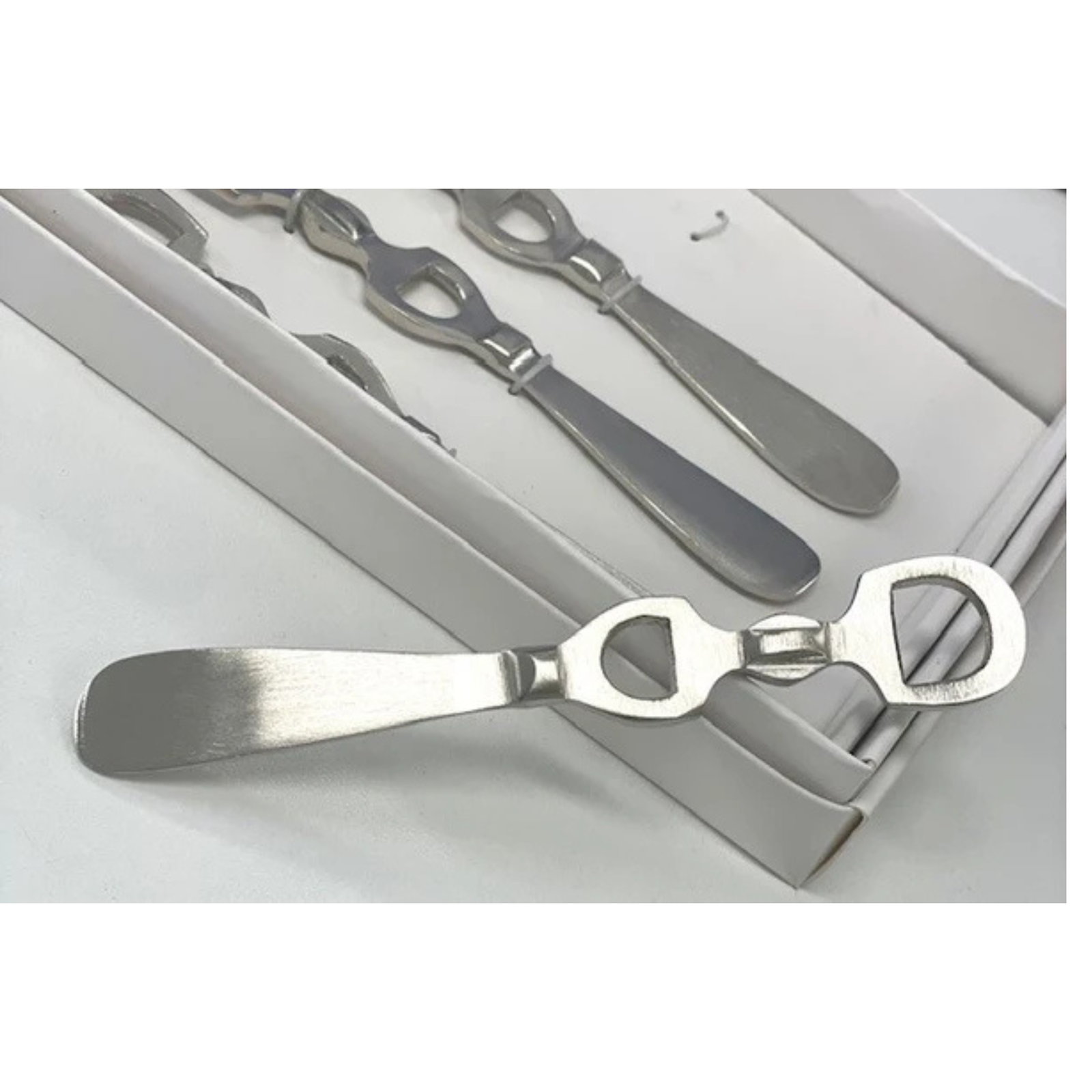 A set of stainless steel bottle openers with a spreader handle, displayed inside and in front of their light gray presentation box.
