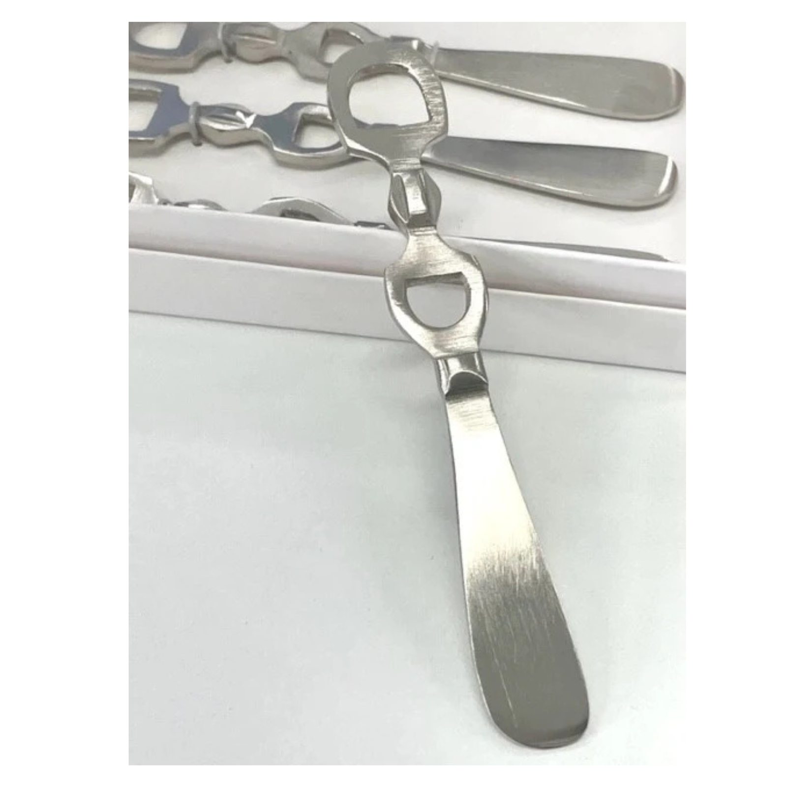 A stainless steel bottle opener with a decorative handle, shown in a close-up product shot with additional similar openers in the background.