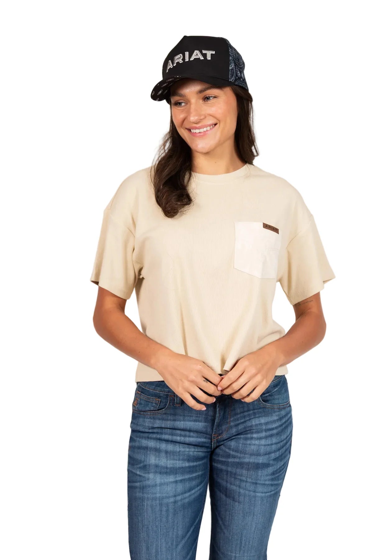 Woman wearing a beige t-shirt, blue jeans, and an Ariat cap on a white background