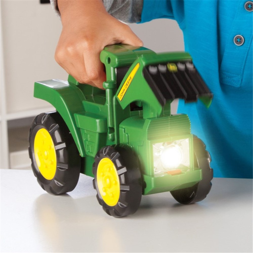 John Deere Tractor Torch . Toy tractor with a light on a white surface, held by a person wearing a blue shirt.