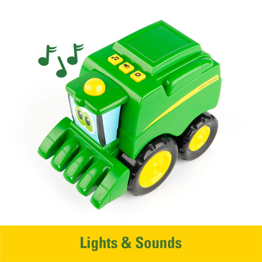 A green toy combine harvester with yellow wheels and buttons, shown on a white background with green musical notes and a yellow banner reading 'Lights & Sounds'.