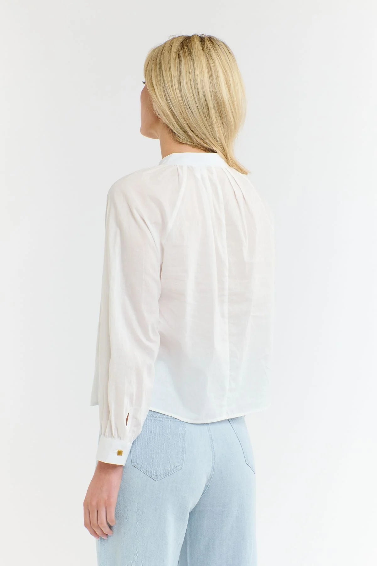 Rear view of a woman wearing a 365 Women's Layla Cotton Top. A white blouse with gold buttons on a white background
