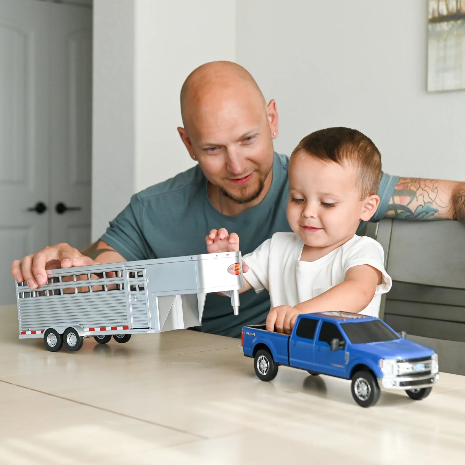 Big Country Sundowner Livestock Trailer. Man and child playing with toy truck and trailer set on a table.