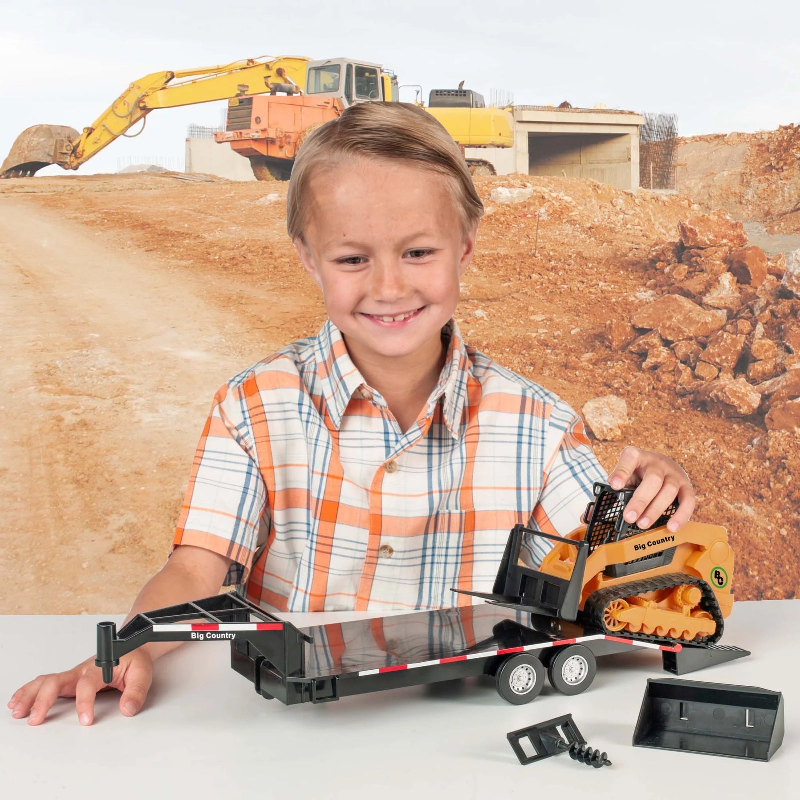 Big Country Toys Track Skid Steer, Trailer & Accessories. Child holding a toy excavator with a construction site background