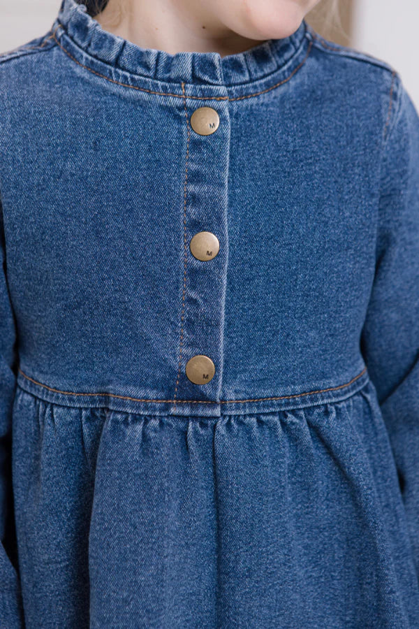 Close-up of a blue denim dress with buttons on a plain background