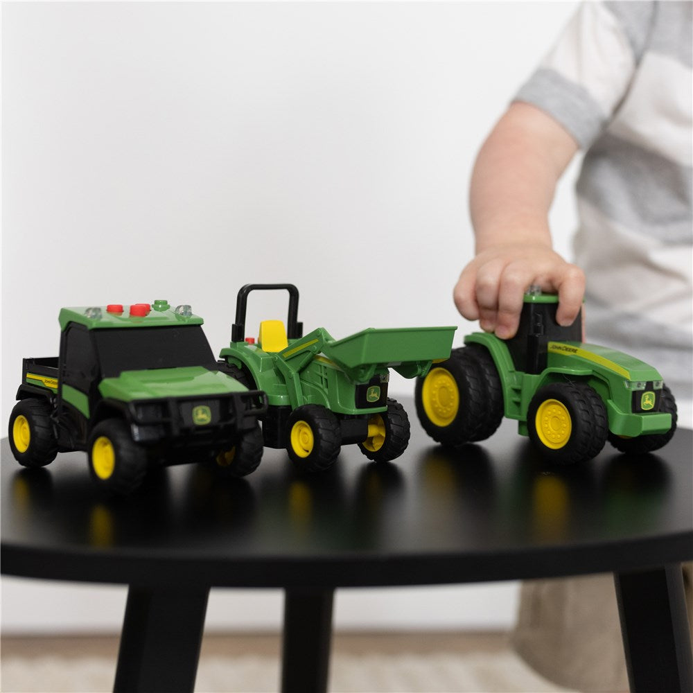 John Deere Lights & Sound Mini Tractors 3-pack. Child playing with toy tractors on a black table