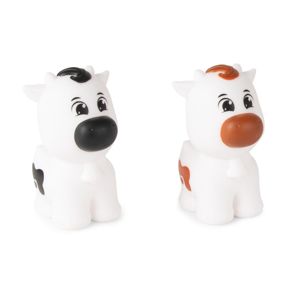 Two small cow-shaped bath toys on a plain white background. One toy is black and white with a black nose and black hair tuft, and the other is white with an orange-brown nose, orange-brown hair tuft, and orange spot.