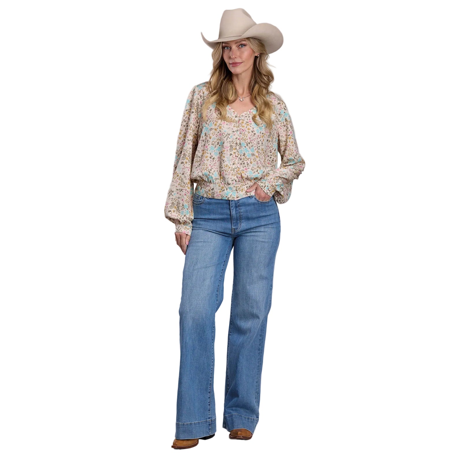 Woman wearing a floral blouse, blue jeans, and a cowboy hat on a plain background