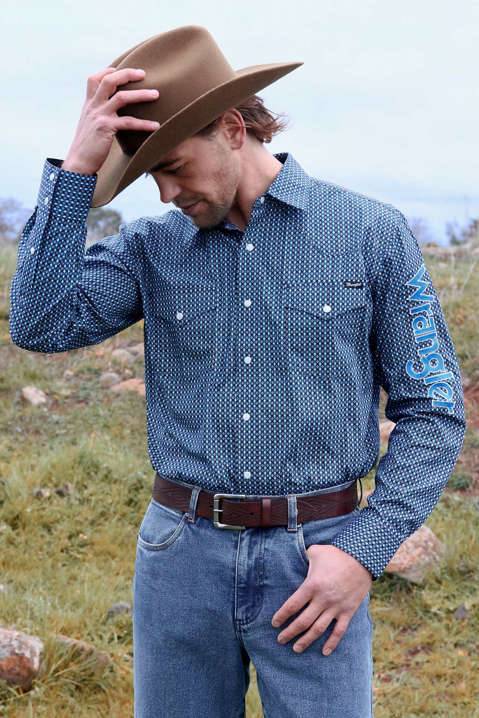 Man wearing a blue patterned shirt and cowboy hat in an outdoor setting