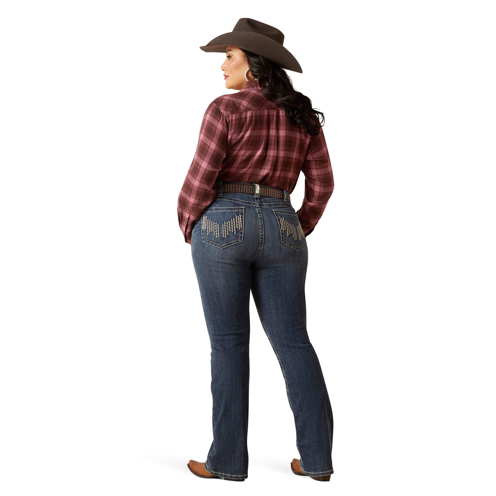 Ariat Women's Halyn Perfect Rise Plus Jean. A woman wearing Ariat women's halyn perfect rise plus jeans with rope-inspired stitching on the back pockets, a plaid shirt, and a hat.