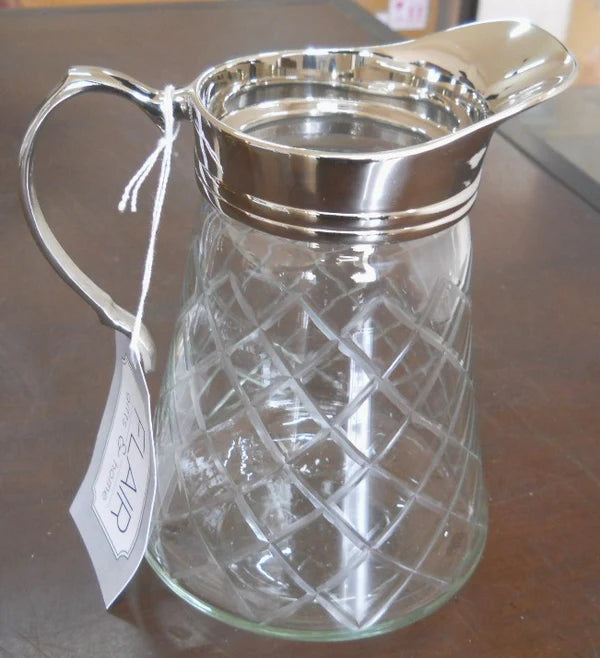Clear glass pitcher with silver lid on a reflective surface
