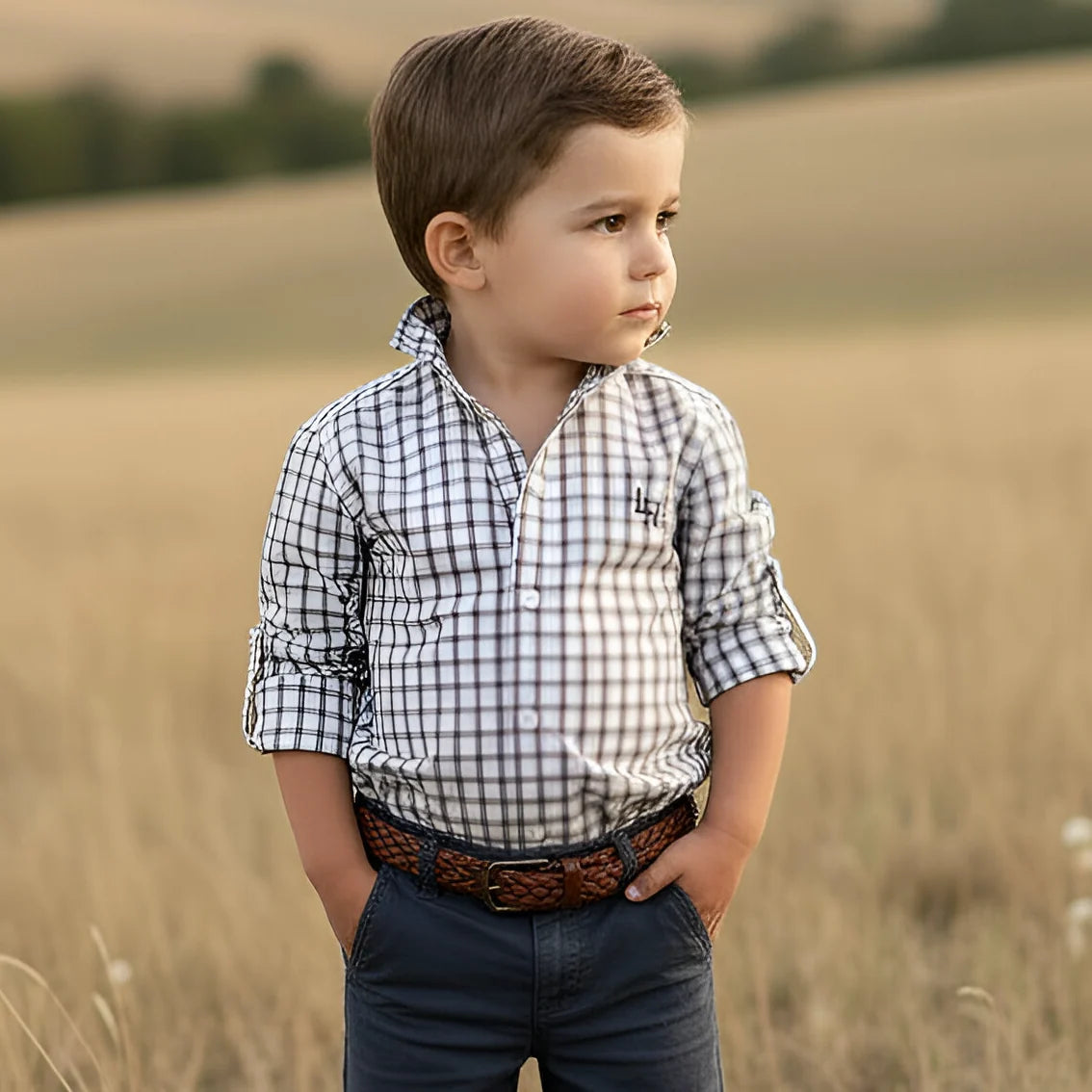 Young boy standing in a field wearing a checkered shirt and jeans.
