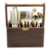 A wooden cutlery organizer caddy with a handle, holding gold-toned flatware and a small bottle on a white background.