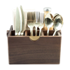 A dark brown wooden cutlery organizer holding gold-toned flatware, including forks, knives, spoons, and napkins, with a small bottle behind it on a white background.
