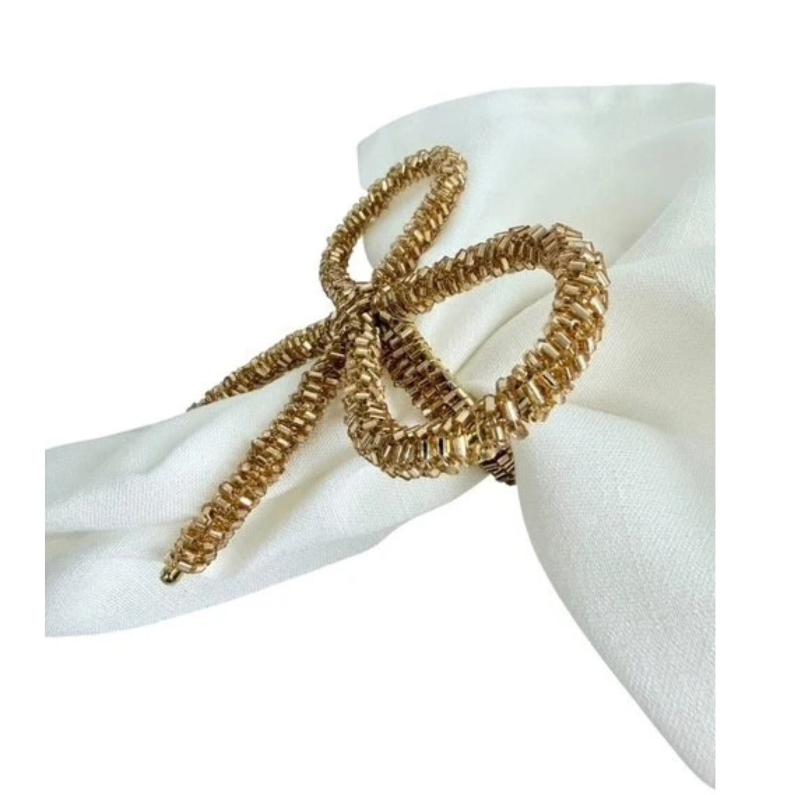 A gold metallic twisted rope napkin ring tied in a bow shape, displayed on a white fabric napkin against a white background.