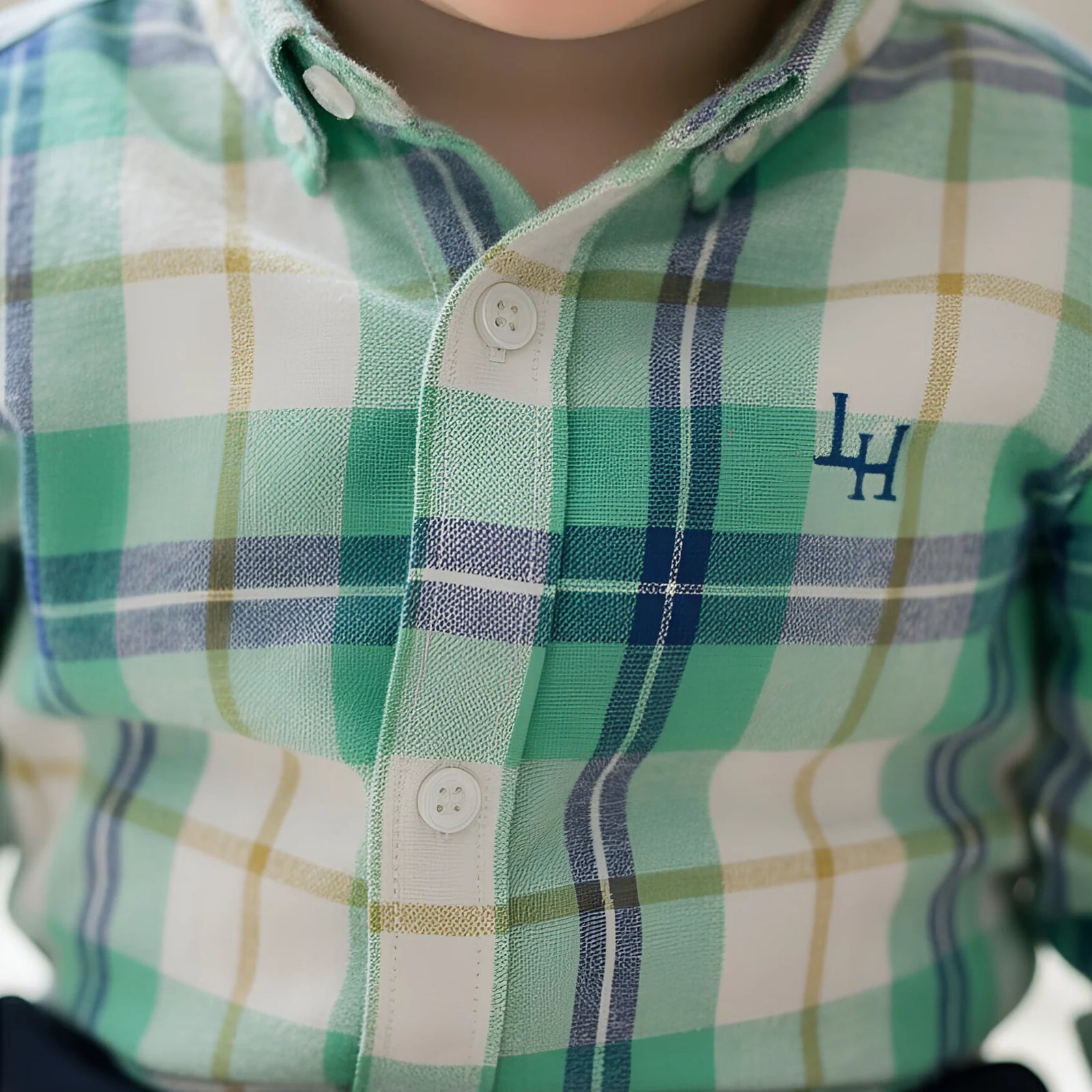 Close-up of a child wearing a green, white, and navy plaid button-down shirt with a blue embroidered 'LH' logo on the chest.