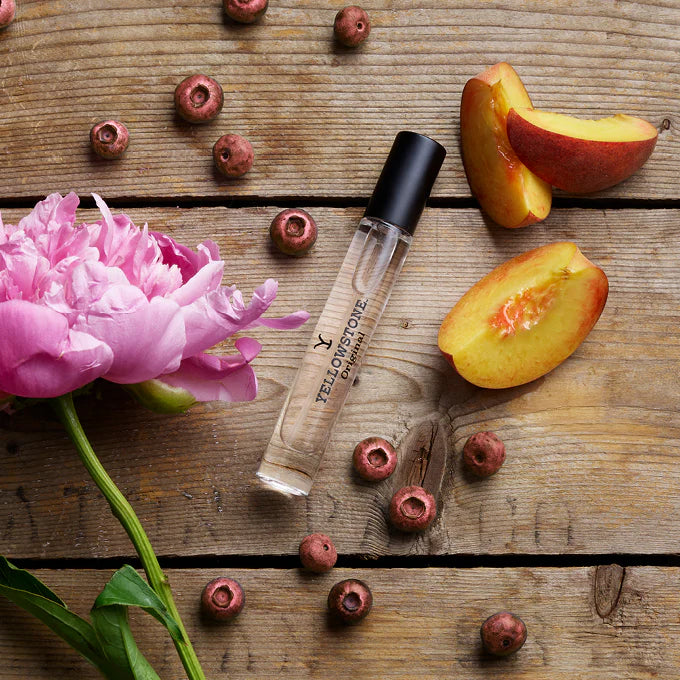 Yellowstone Parfum bottle with peaches and a pink flower on a wooden surface