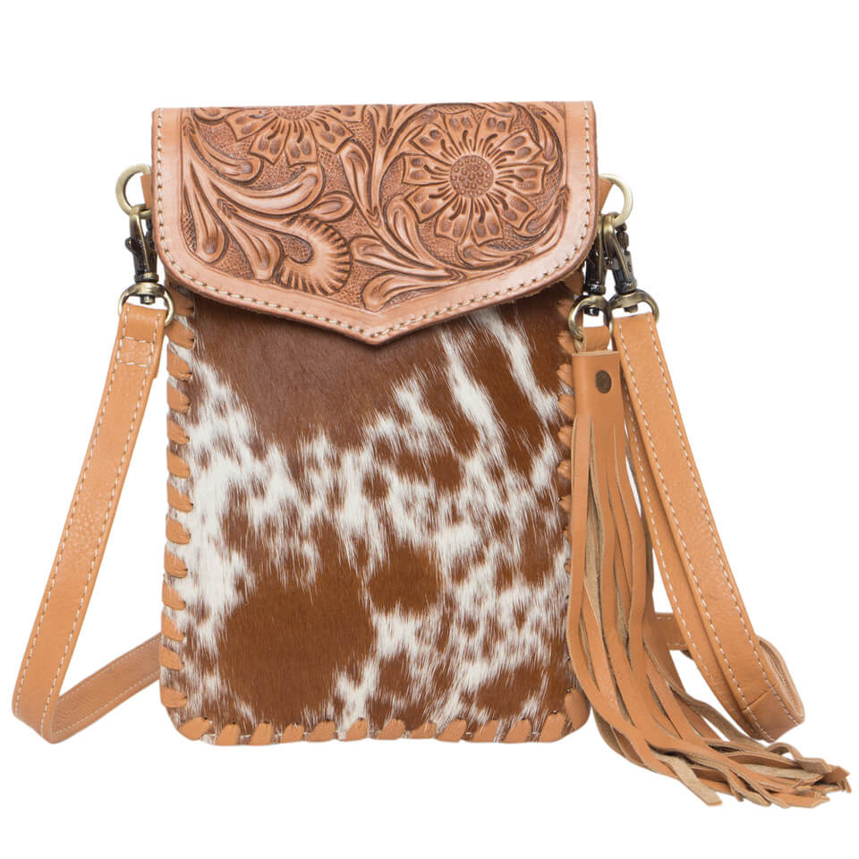 Women's Tooling Cowhide Phone Bag. A brown and white cowhide leather phone bag with hand tooling details, a magnetic closure, and a detachable leather tassel. It includes a shoulder strap and zipper back panel.