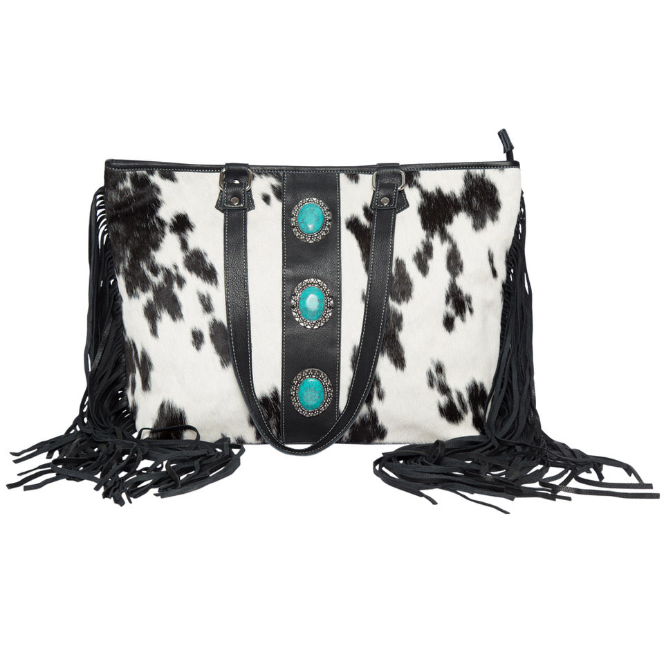 Women's Big Cowhide Bag With Turquoise Stonework and Fringes. A cowhide handbag featuring turquoise stonework and fringes on the sides. It has a black and white patterned cowhide leather exterior, multiple shoulder straps, and is displayed in a flat position.