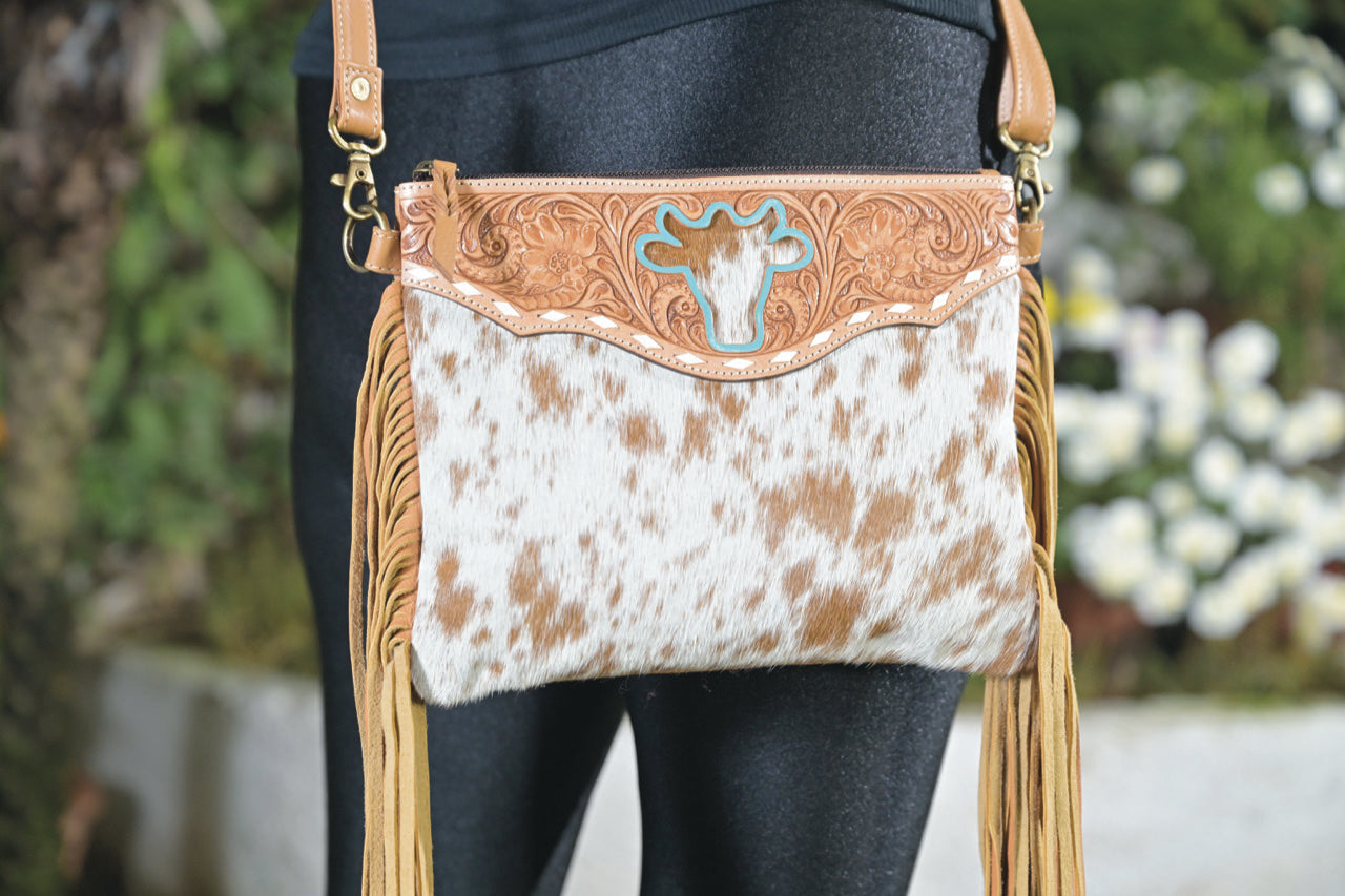 Women's Marbella Bullhead Cowhide Sling Bag with Fringes. A woman's sling bag with a fringed design and intricate hand carving, showcasing a beige and brown color scheme.
