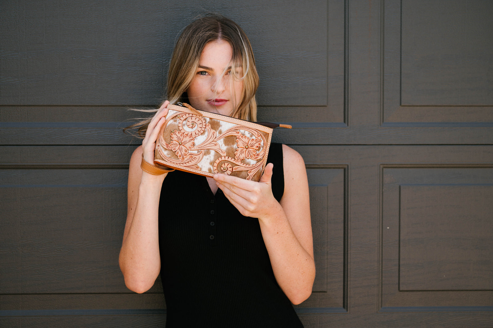 Woman holding a decorative clutch in front of a dark wooden door