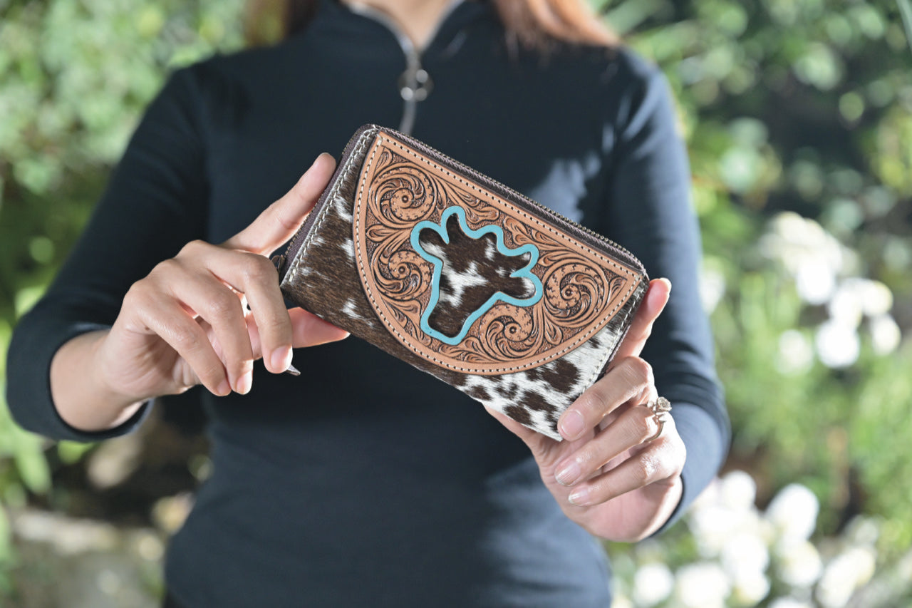The Design Edge Women's Ronda Bullhead Wallet. A person holding a brown and black cowhide leather wallet with a bullhead design and zipper closure.