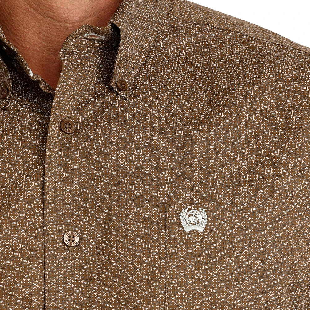 Close-up of a brown short-sleeve button-down shirt with a small white geometric pattern and a white embroidered chest logo, worn by a model.