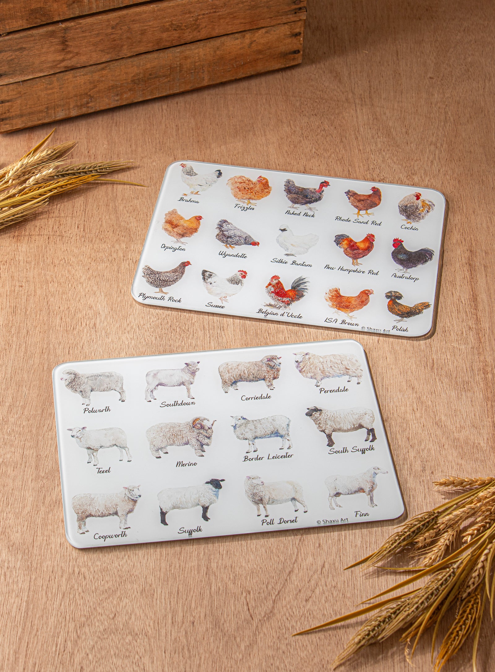 Two placemats with animal illustrations on a wooden surface with wheat stalks.