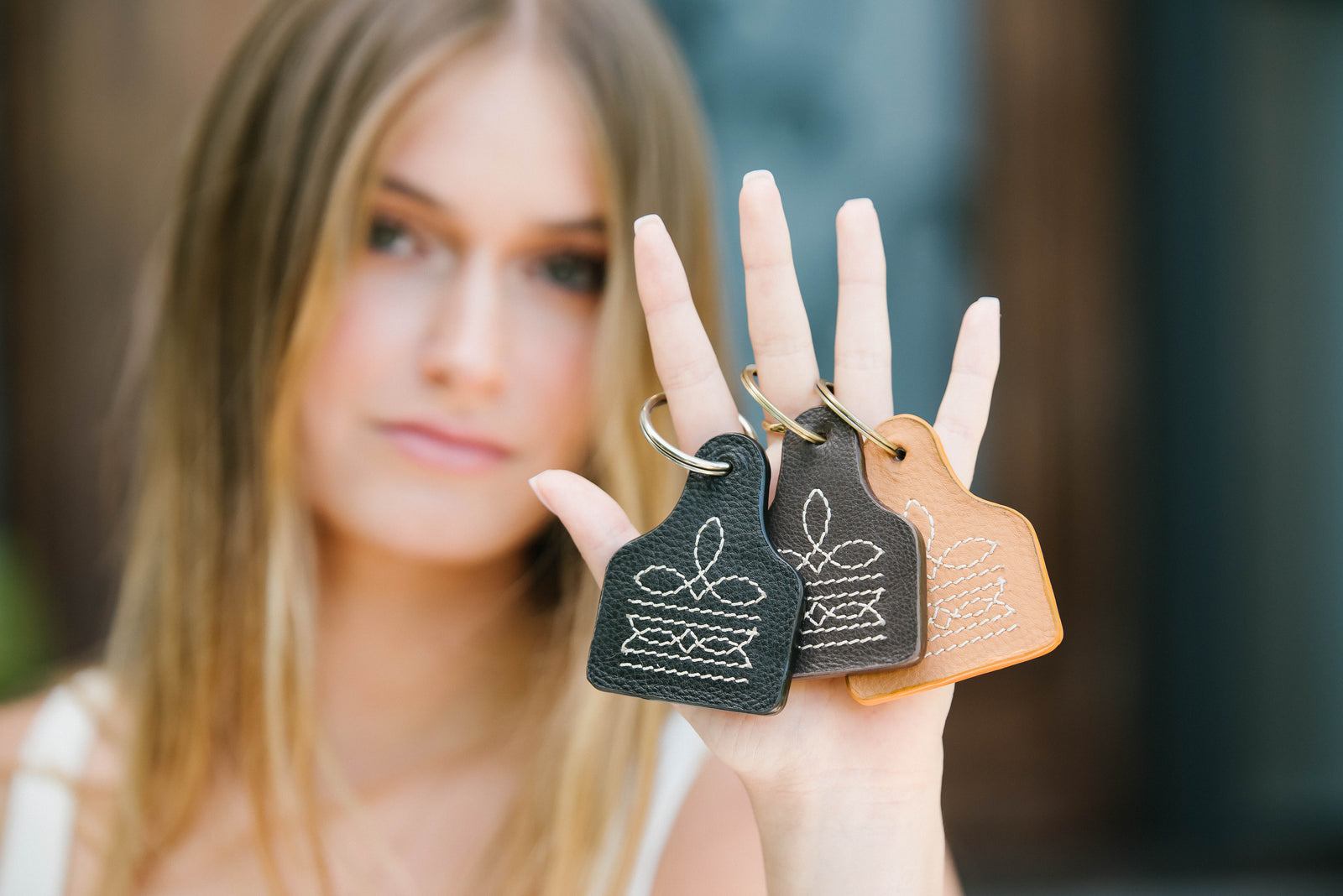 Woman holding two leather keychains with floral designs.