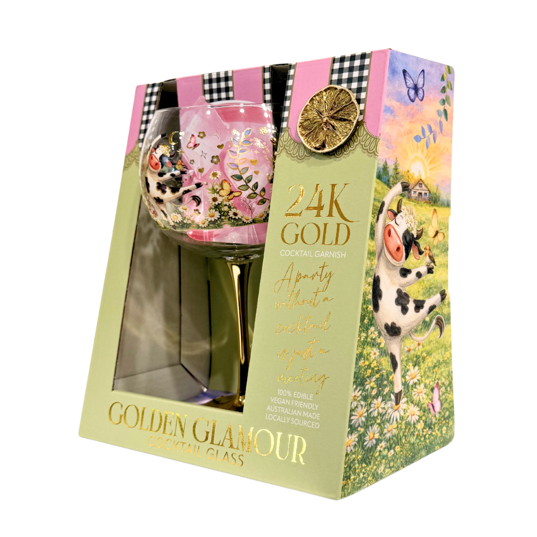 A boxed cocktail glass set on a plain white background. The package is pastel green with pink and black gingham accents, gold lettering, and a printed illustration of a cow in a flower field.