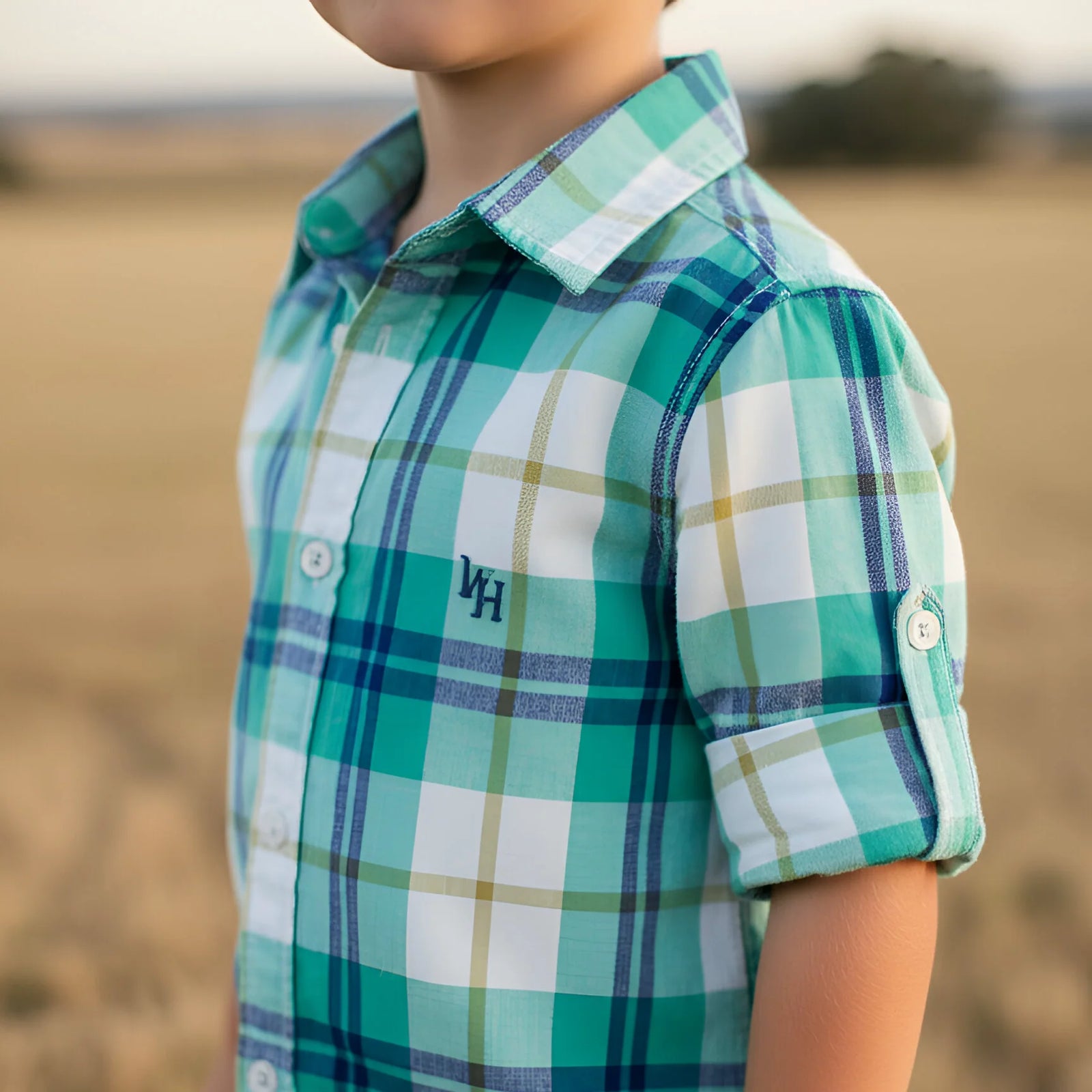 Child wearing a green plaid shirt with a logo in an outdoor setting