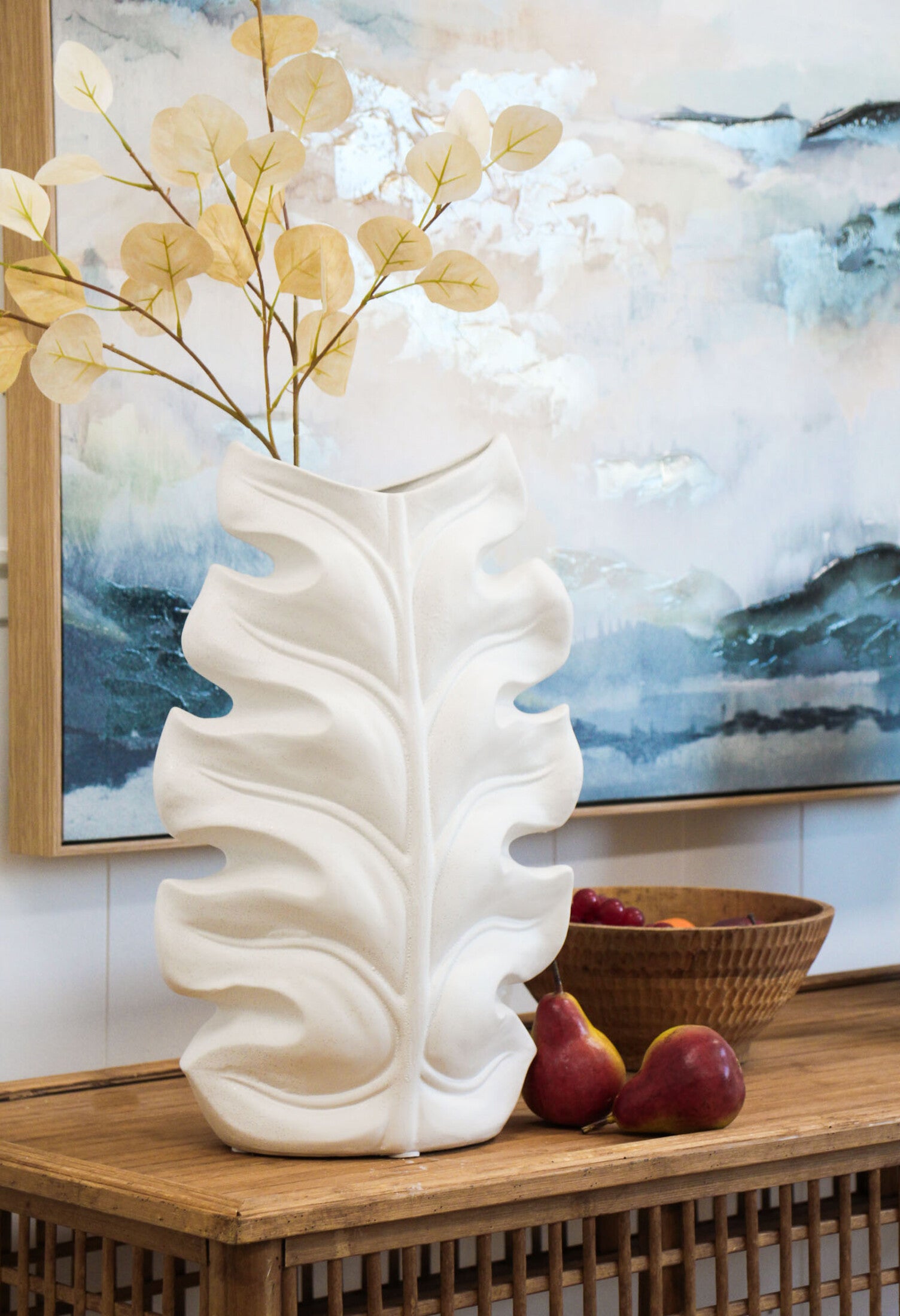Rustic White Leaf Vase. White decorative vase on a wooden surface with a painting in the background