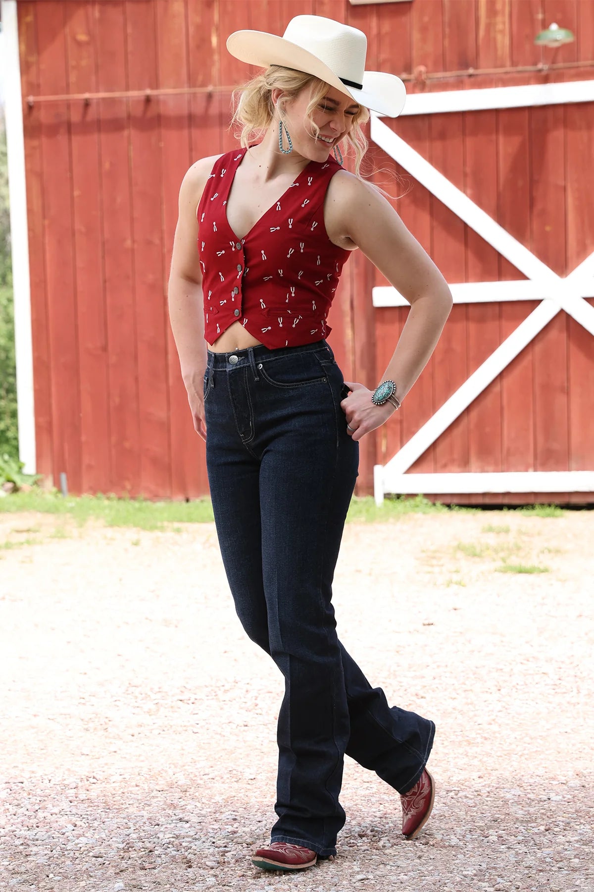 Woman in a red patterned top and black jeans standing in front of a red barn.