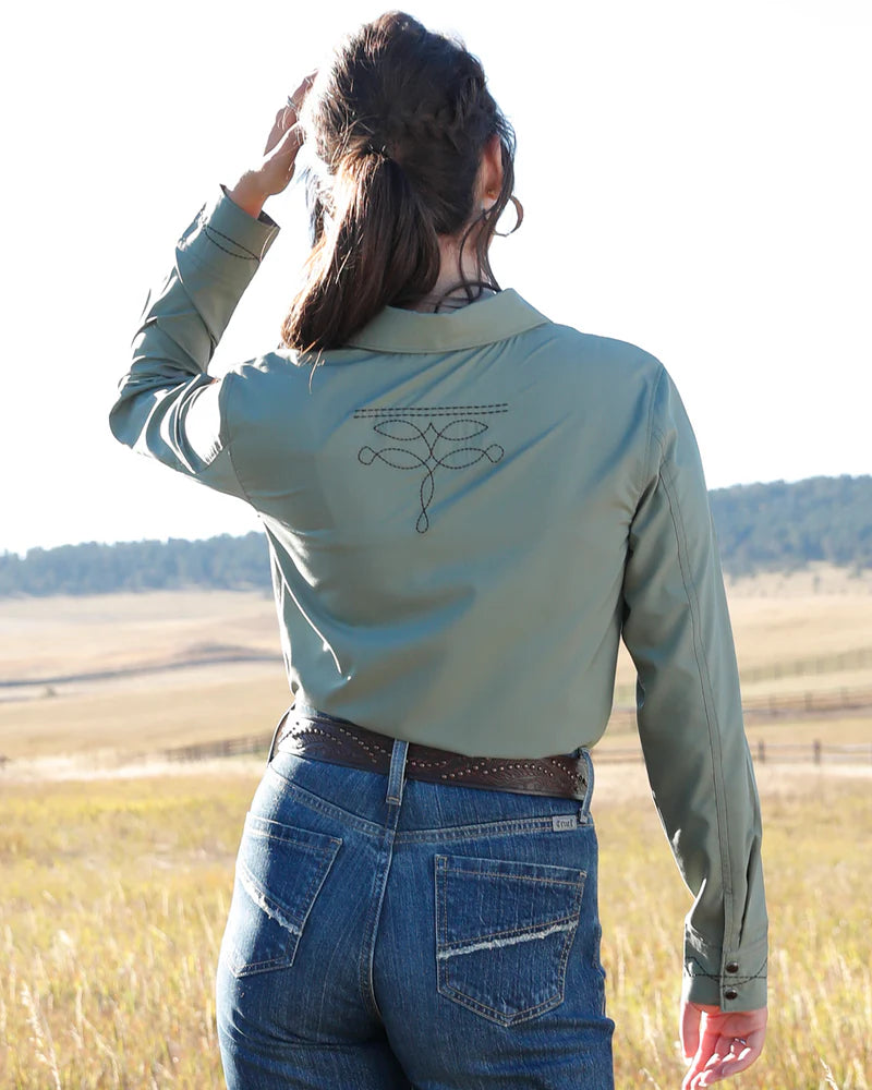 Person wearing a light green jacket with a logo on the back, standing in a field.