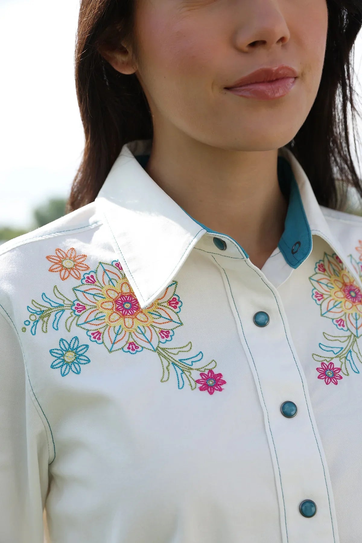 Close-up of a person wearing a white blouse with colorful floral embroidery.