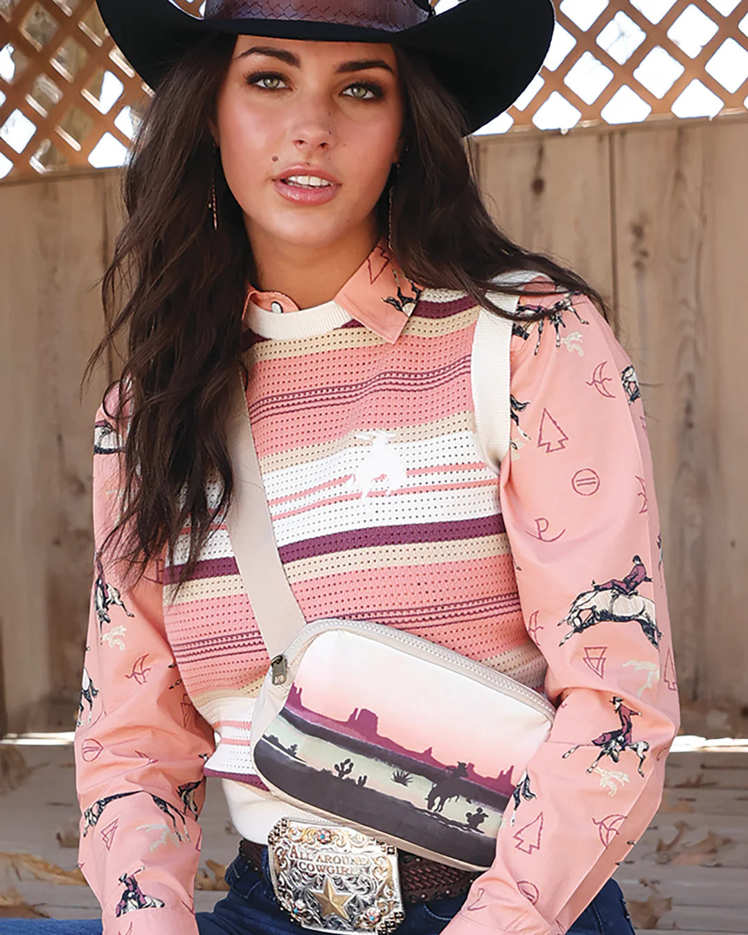 Woman wearing a pink patterned shirt with a cowboy hat and carrying a white bag with horse designs.